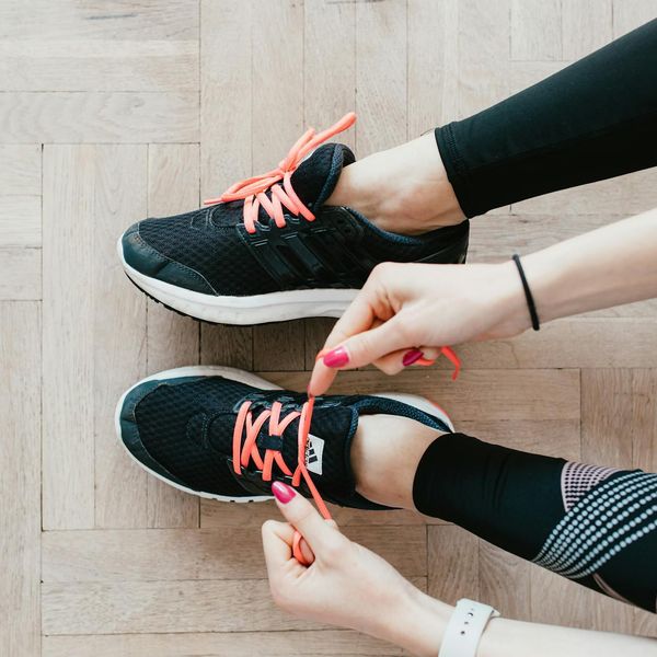 A child's sports shoes and a water bottle placed on a wooden floor.